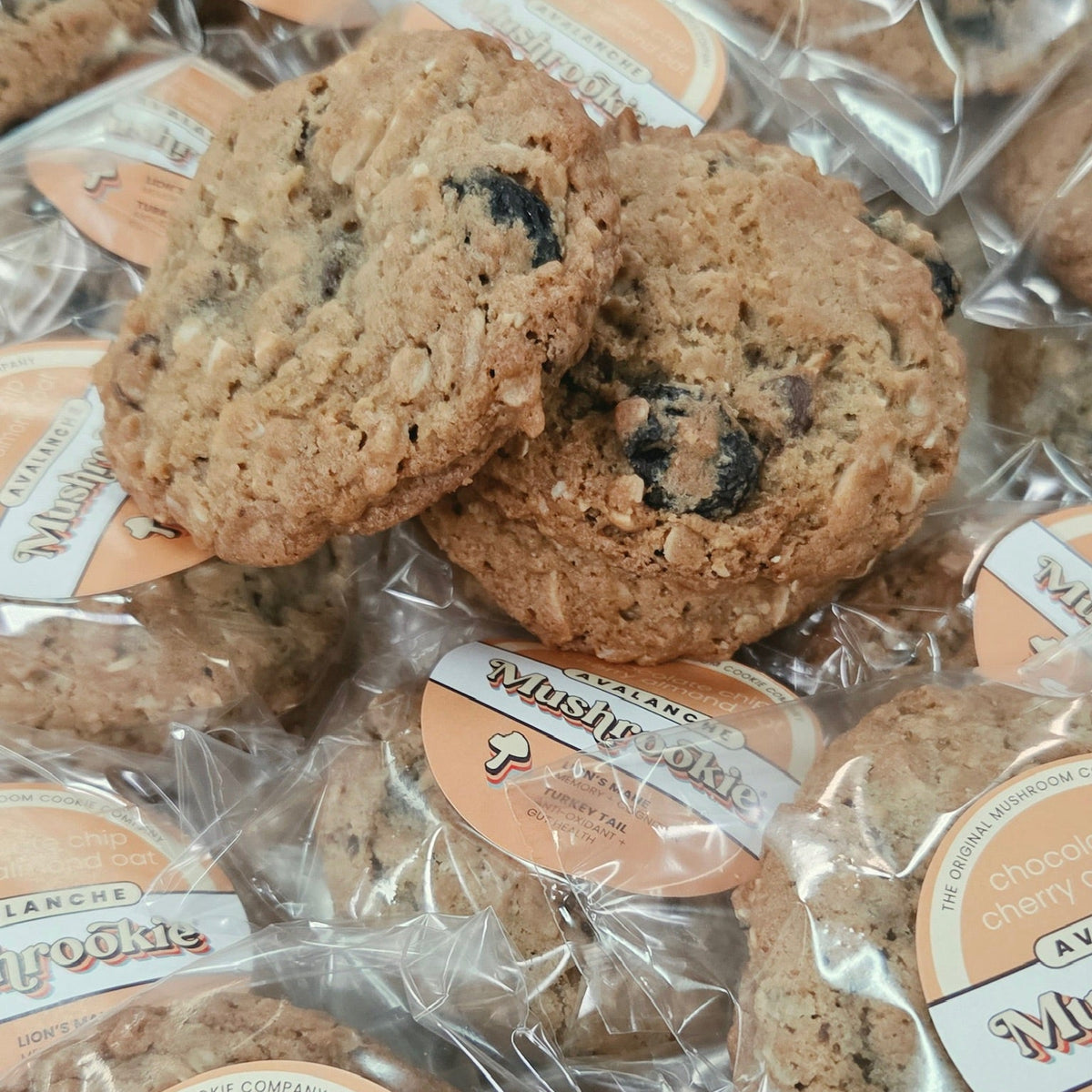 A close-up pile of packaged chocolate chip cookies in clear plastic bags with round peach-and-white labels. The label reads 'Avalanche.'