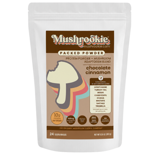 A white stand-up pouch of Mushrookie Packed Powder chocolate cinnamon mushroom powder and mushroom blend, featuring a brown label with a mushroom graphic and serving size 24.