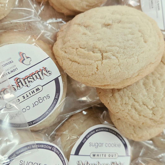 Several round sugar cookies in clear plastic bags with white circular labels reading 'Mushroom Cookie' and 'White Out'.